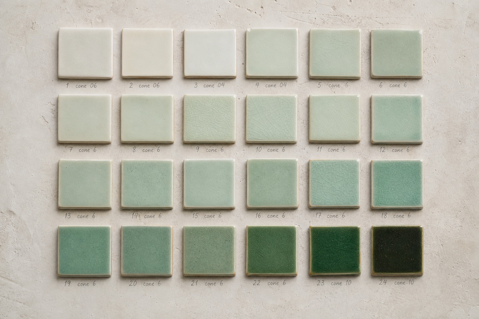 A grid of two dozen ceramic test tiles in shades of celadon, from near-white to deep jade, each numbered in pencil
